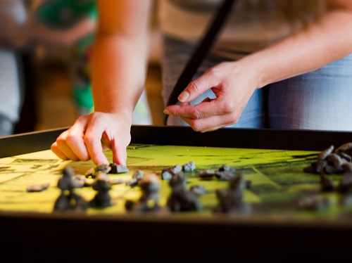 Eine Person streckt die Hand aus, um kleine Figuren in einem Brettspiel zu bewegen.